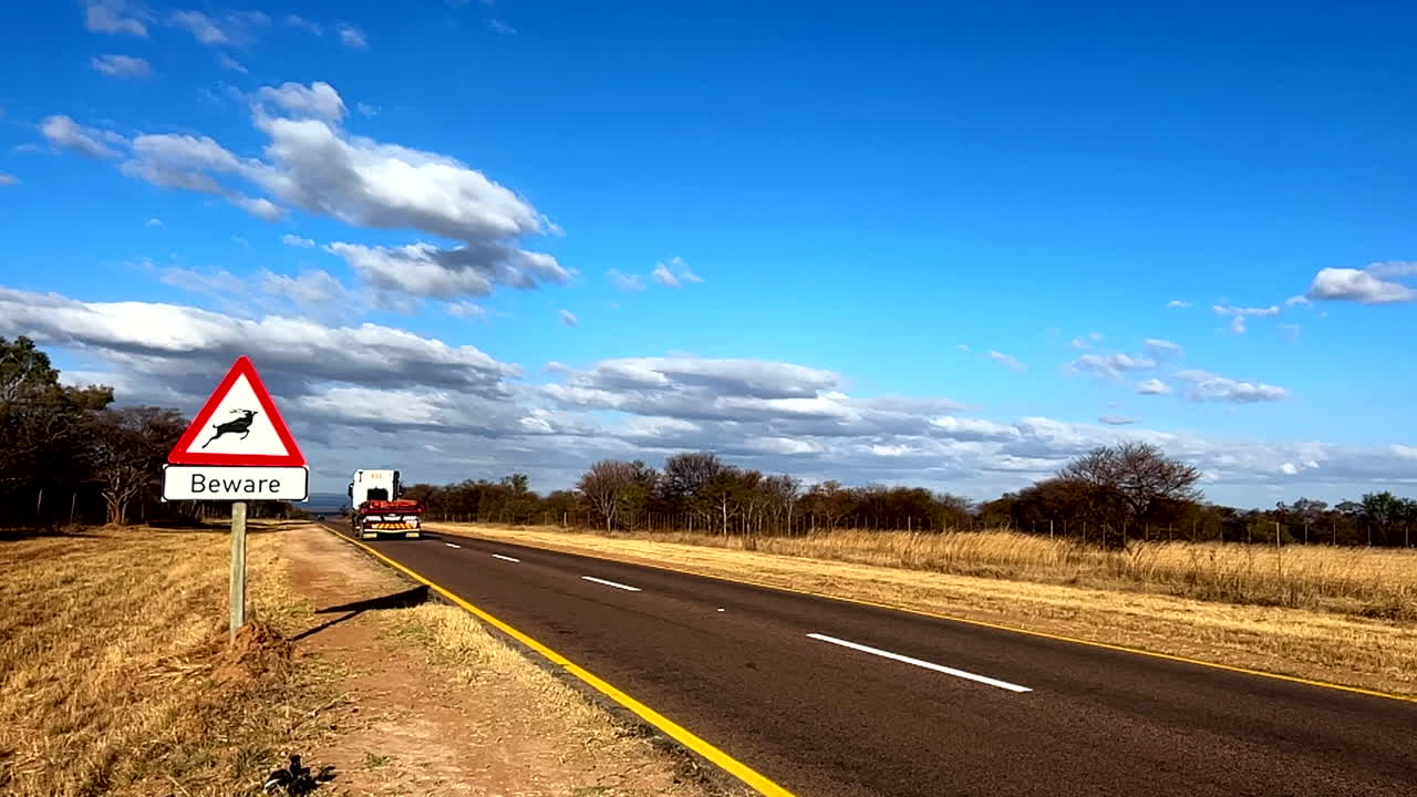 Beware road sign for kudu next to highway as truck drives past, slow motion