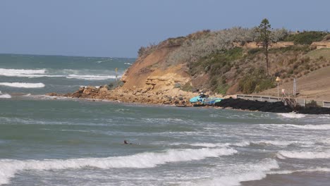 A surfer rides waves near a scenic cliff on a sunny day. The video captures dynamic ocean movement and vibrant coastal scenery