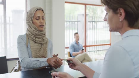 Biracial-woman-paying-with-credit-card-at-reception-at-modern-dental-clinic