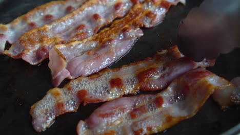 hombre chef cocinando para el desayuno, convirtiendo un increíble tocino crujiente, rico en grasa y color, chisporroteando y fumando en una sartén caliente