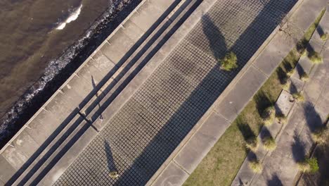 Isolated-and-unrecognizable-man-walking-along-river-on-concrete-pavement-with-geometric-shapes,-Buenos-Aires-in-Argentina