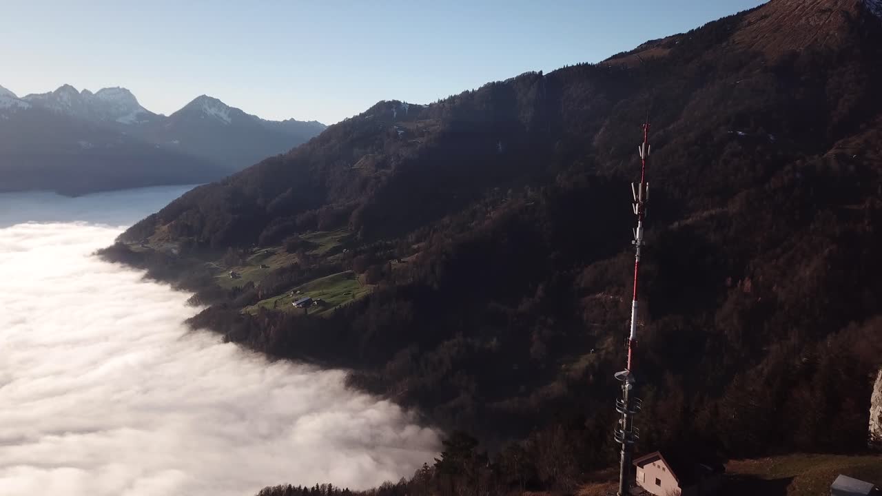 pequeña estación transmisora con un mástil de telecomunicaciones en la ladera de una montaña sobre una cubierta de nubes en el valle