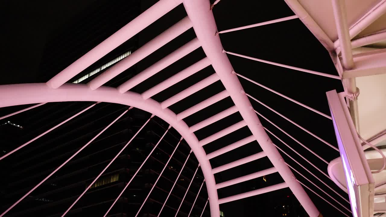 Camera tilts upward revealing illuminated Silom Bridge architecture against night sky, urban Bangkok environment