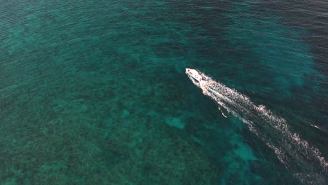 lancha blanca navegando en una superficie clara de mar turquesa con arrecifes de coral hacia una isla