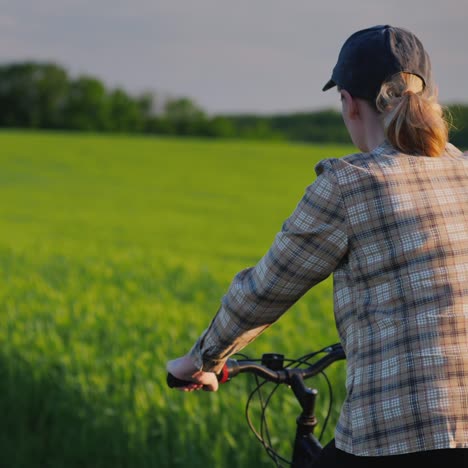 Mujer-Monta-Su-Bicicleta-Entre-Campos-De-Trigo-Verde