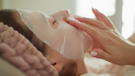 lady applies facial mask lying in spacious place. young brunette female in bathrobe strokes skin nourishing mask with finger in room slow motion