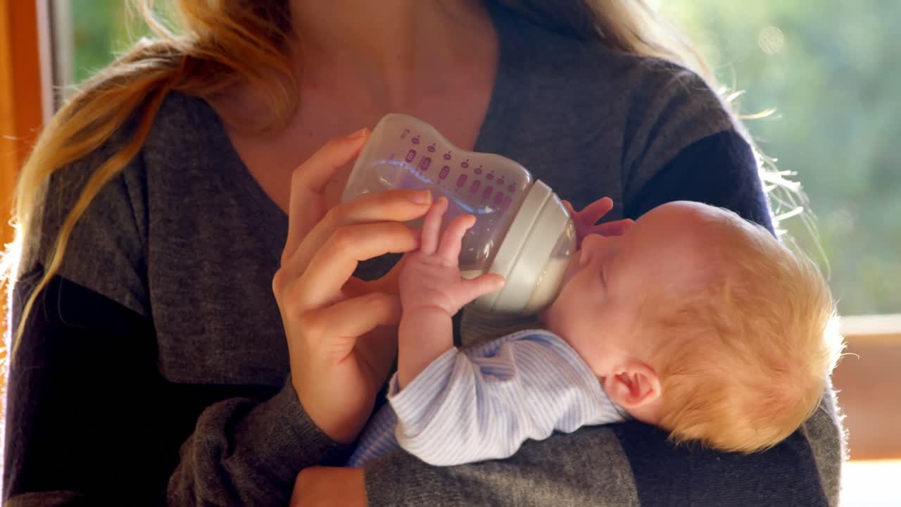 madre alimentando leche a su bebé en la sala de estar 4k