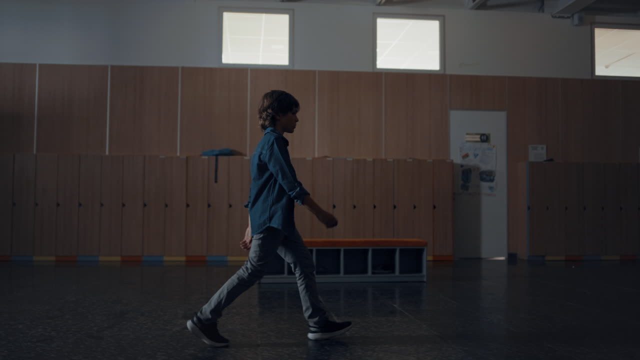 Relaxed pupil walking dark school hall alone. Teen schoolboy passing lockers.