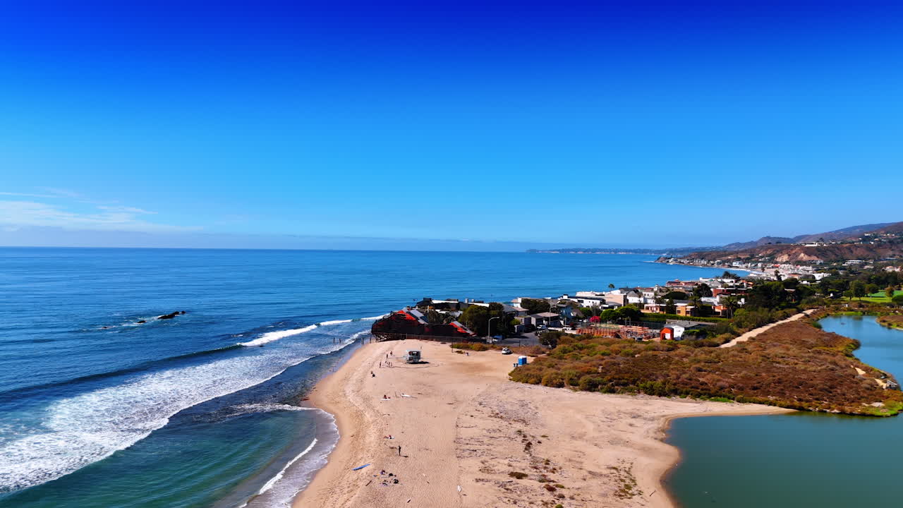 Few people having rest on the sandy beach of the Pacific Ocean. Aerial perspective on the residential area of Malibu, Los Angeles County, California, USA on sunny day
