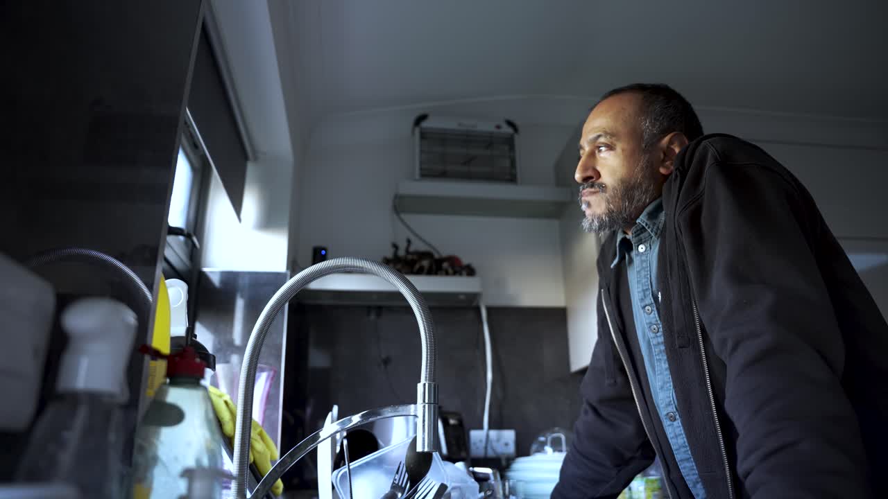 South Asian Man Gazing Out Kitchen Window With Pensive Expression Contemplating Life's Challenges And Future Opportunities In Modern Home Interior