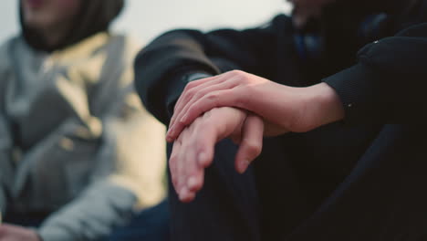 close-up of clasped hands as the person moves them gently, with a blurred background showing another individual wearing a gray top