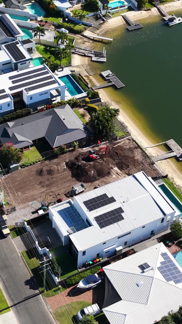High-angle drone shot of modern canal homes and active construction in a coastal neighborhood.