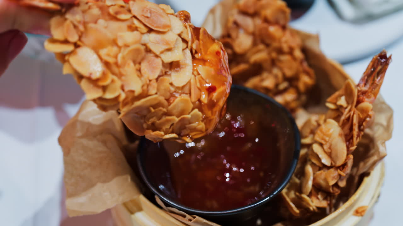 Close up of a woman dipping a crispy, almond-coated fried food into a red sauce