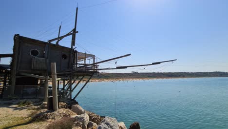 Typical-restaurant-in-Trabucco-fishing-construction-at-Punta-Penna-reserve-beach-and-people-bathing-in-Abruzzo,-Italy