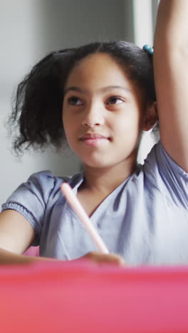 Video of happy biracial girl raising hand during lesson in classsroom