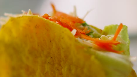 close up details of delicious fresh mexican taco made from crispy corn tortilla filled with variety of ingredients including beef, lettuce, carrot, tomatoes and cheese. latin american food cuisine