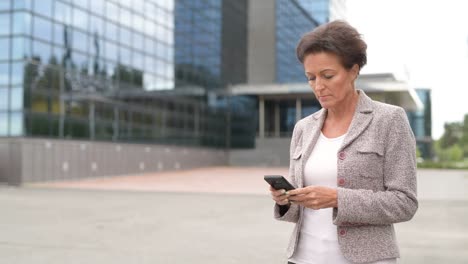 mature beautiful businesswoman using phone in the city outdoors