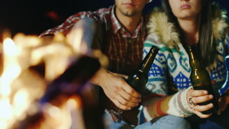 pareja joven relajándose junto al fuego bebiendo una cerveza o una bebida de la botella