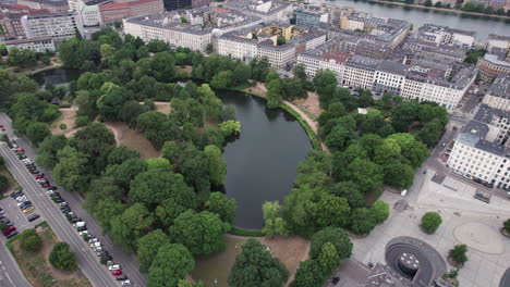 the aerial perspective reveals ørstedsparken, a serene oasis of green trees and lakes amidst the urban landscape of central copenhagen