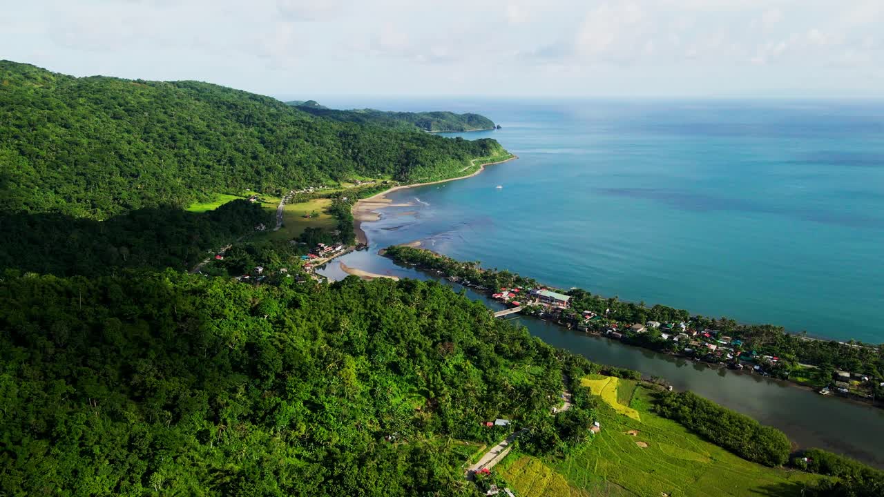 Panoramic view of vibrant, lush hillside barangay town facing turquoise cove at Batalay, Bato, Catanduanes - aerial forward shot