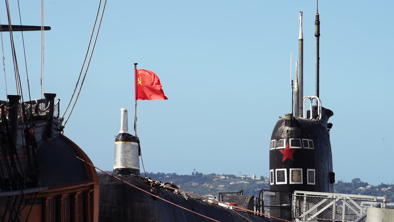 Historic submarine with a red Soviet flag and star insignia docked in port under clear sky