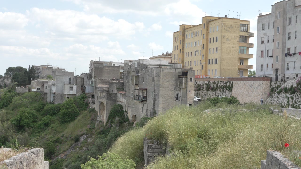 Uma vista panorâmica mostrando o contraste entre edifícios históricos de pedra e apartamentos modernos situados na beira de um penhasco verde na Província de Matera, Itália