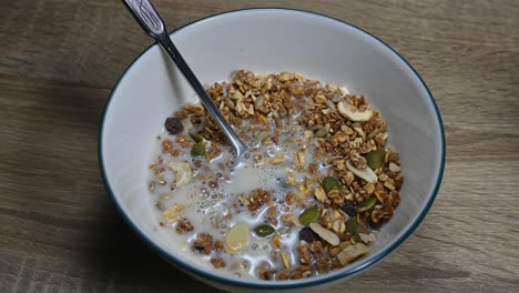 aleje la granola en un tazón con una cuchara y leche de almendras recién vertida para hacer burbujas, semillas, frutas secas, desayuno saludable