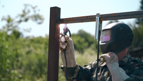 constructor en camuflaje suelda la tabla superior de la nueva valla en el día