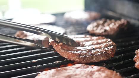 primer plano extremo en cámara lenta de una hamburguesa humeante y jugosa volteada con pinzas en una parrilla de fuego