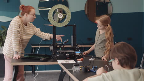 teacher explaining schoolgirl how 3d printer works