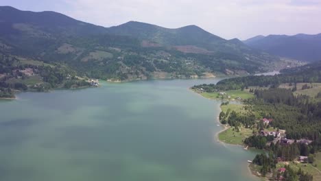 Panorámica-Aérea-Lenta-Hacia-Arriba-Del-Agua-Del-Lago-Con-Sombras-De-Nubes-Y-Bosques-Verdes