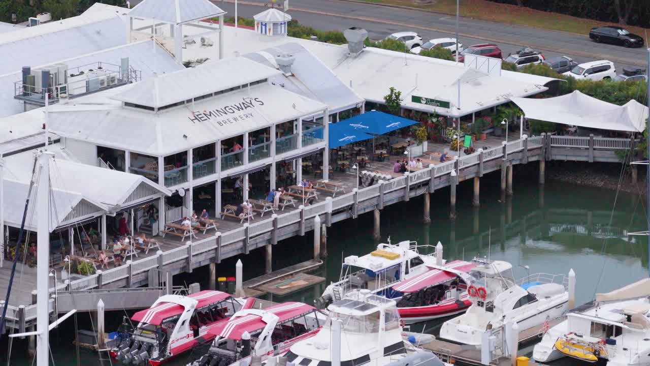 Aerial view of a bustling marina with boats and a lively waterfront restaurant in Port Douglas, Australia