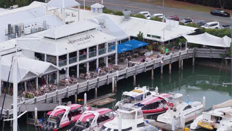 aerial view of a bustling marina with boats and a lively waterfront restaurant in port douglas, australia
