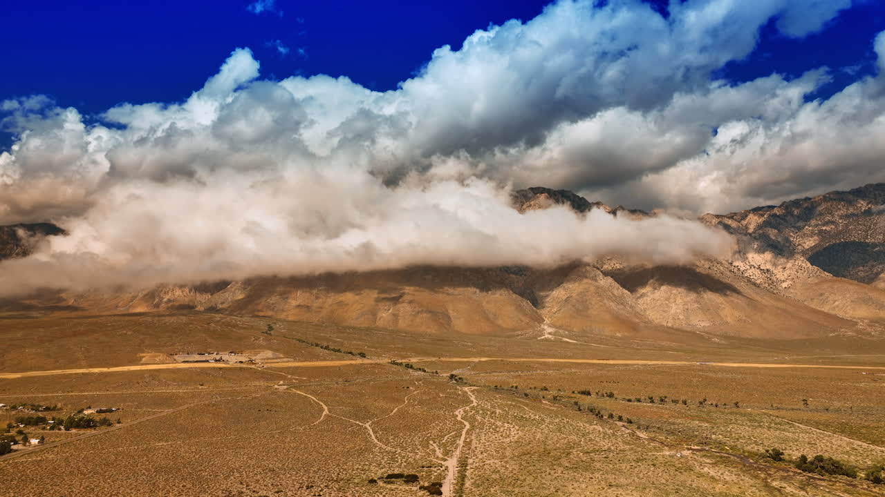 White cloudscape hiding the tops of the mountains. Dry deserted land at the foot of the rocks. Aerial perspective on Death Valley.