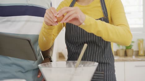 Mid-section-of-diverse-couple-using-tablet-and-baking-in-kitchen