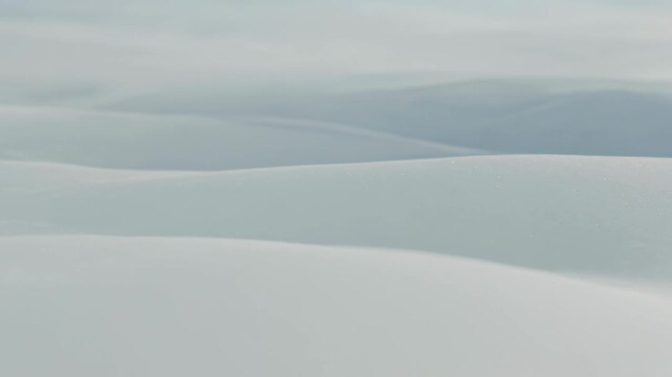 Drifting camera revealing expansive pale rolling ridges in remote field, showing diffuse cloudy sky