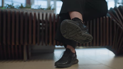 close up of seated lady tapping foot rhythmically to music with legs crossed, wearing black sneakers. scene focuses on shoe sole detail and subtle motion, set indoors with soft natural lighting
