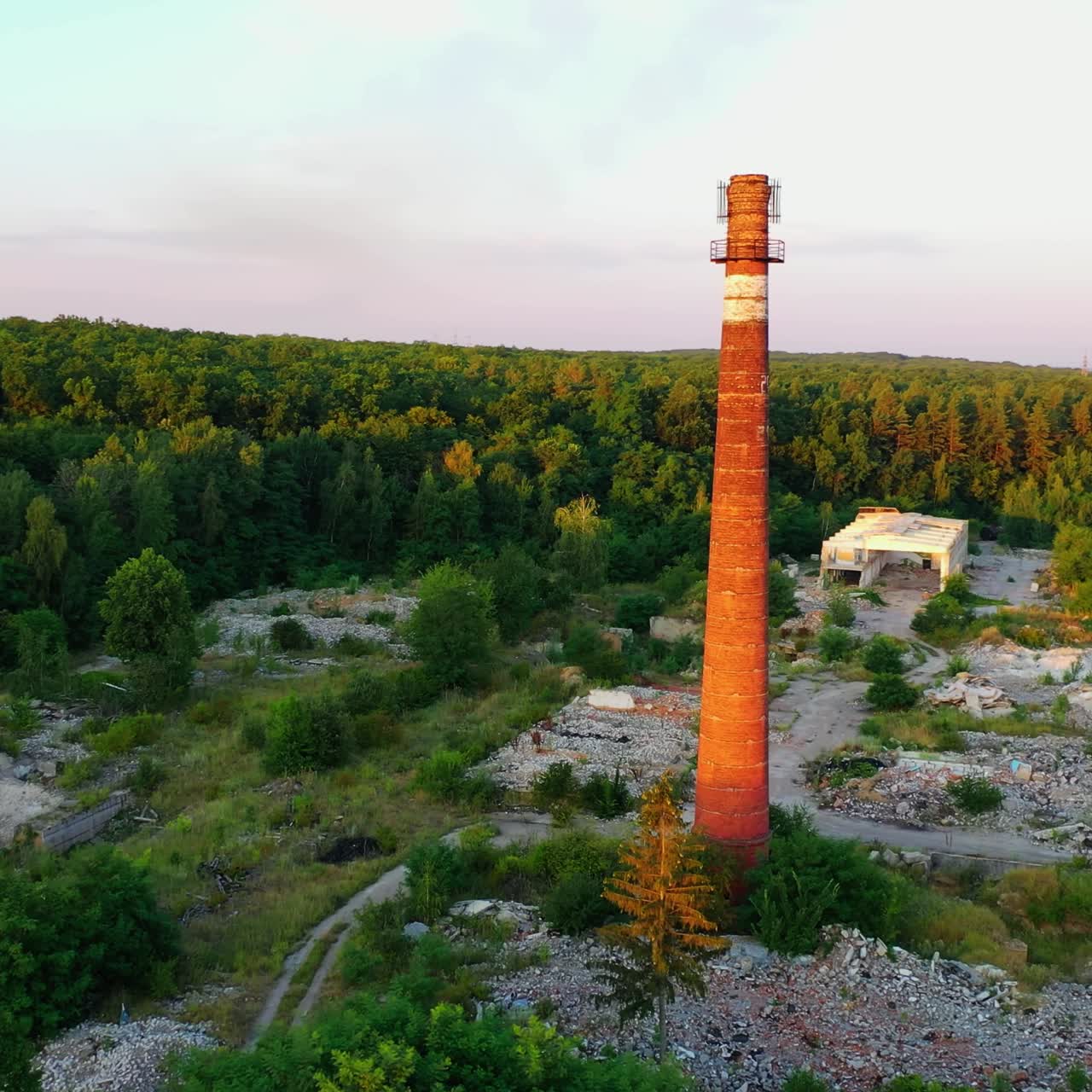 Old brick pipe among nature. Tall factory tower on abandoned place in the countryside in bright summer day. Aerial view.