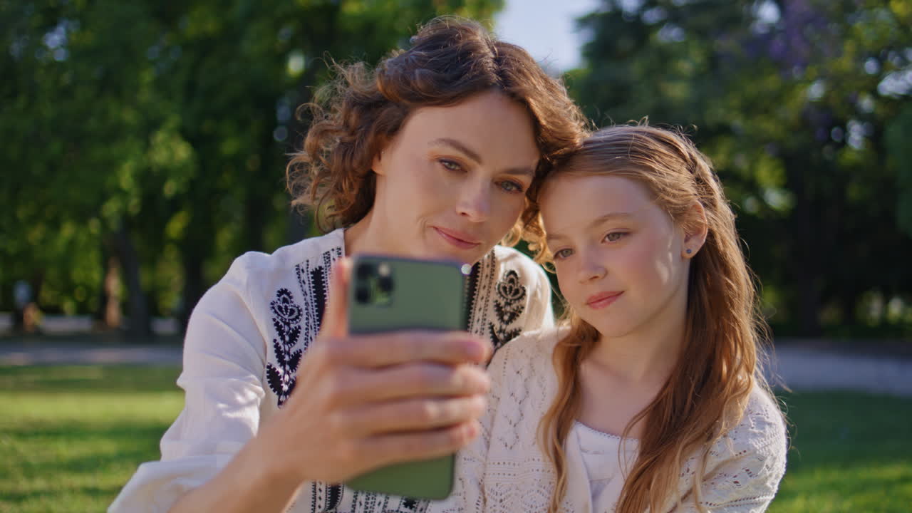 Smiling mother streaming daughter on nature using smartphone. Mom child bonding