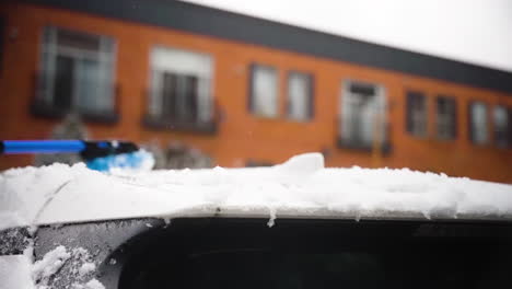 detail of car roof being cleaned wiping snow off with steady hand motion, apartment building backdrop