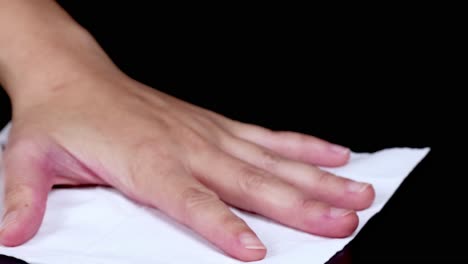 a hand smoothly moves a white cloth across a dark surface, demonstrating a cleaning motion.