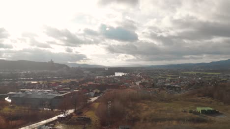 forward aerial drone through trees over outskirts of small city with silhouette castle on hill in background