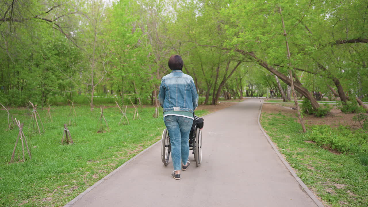 Caretaker Wheels Ahead, Assistance Provider Guiding Wheelchair Along Tranquil Park Trail, Compassionate Caregiver Steadily Propels Wheelchair Along Peaceful Paved Park Pathway Surrounded By Trees