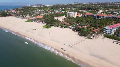 drone orbits from left to right over mui ne beach, keeping rental bucket boats in center frame, with seaside resorts and horizon in the background.