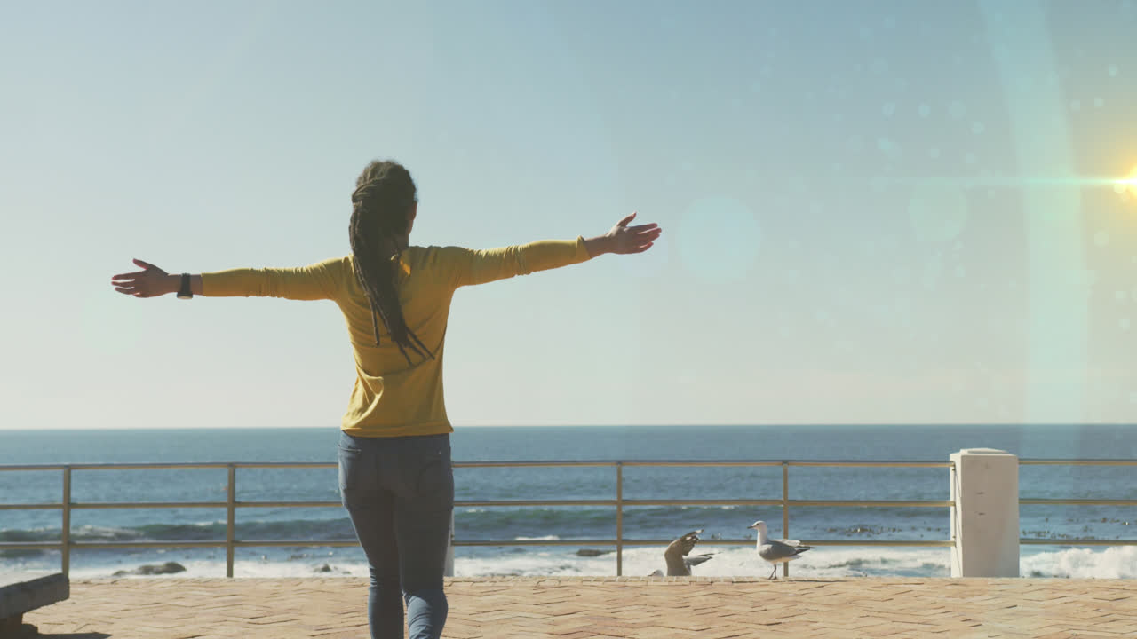 산책로에서 팔을 넓게 펴고 있는 아프리카계 미국인 여성의 뒷모습에 대한 빛의 반점