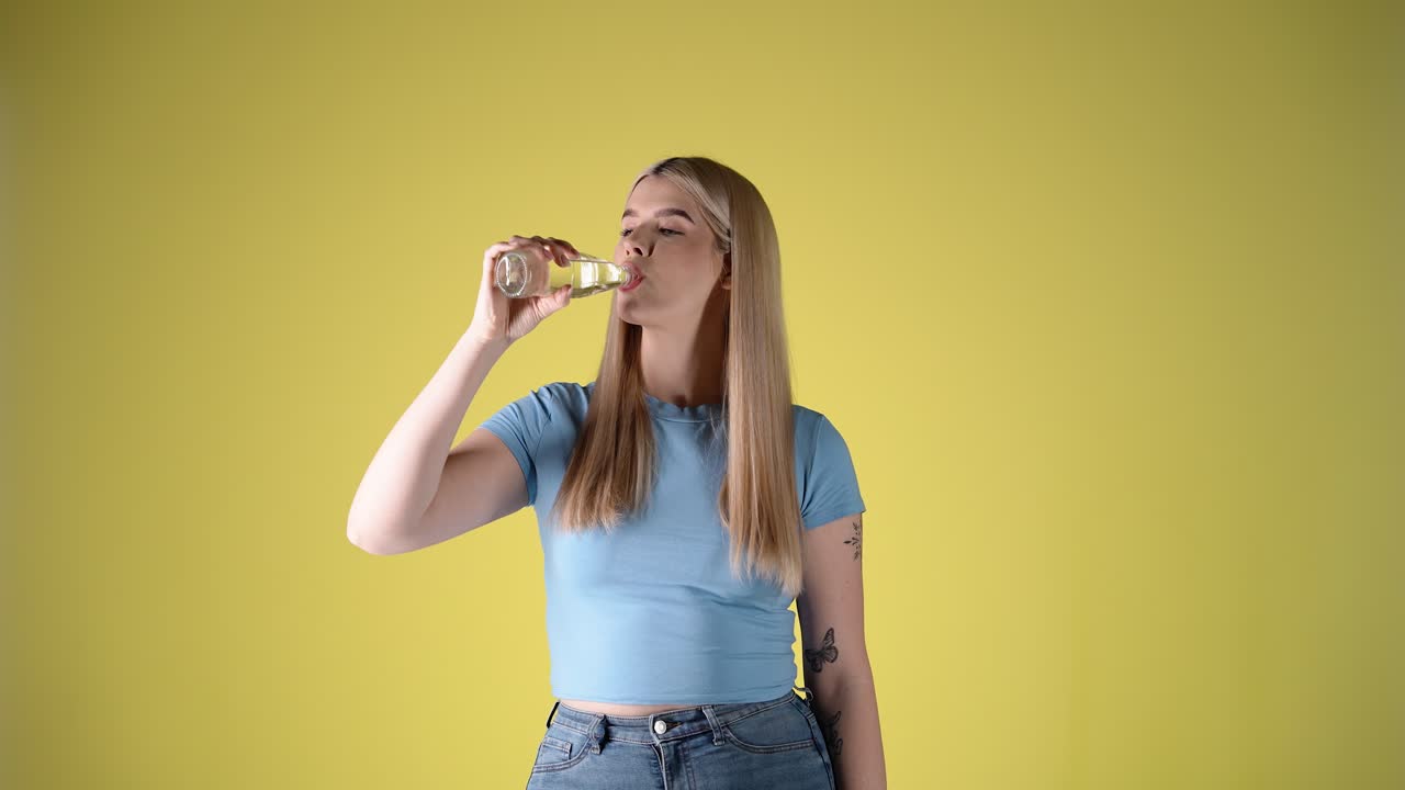 Cute woman looking at camera and taking a sip out of glass bottle, happy smile