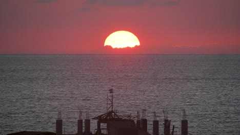 Red-sun-setting-in-the-sea-in-Gaza-with-Israel-flag-in-front,-dramatic-sunset-footage