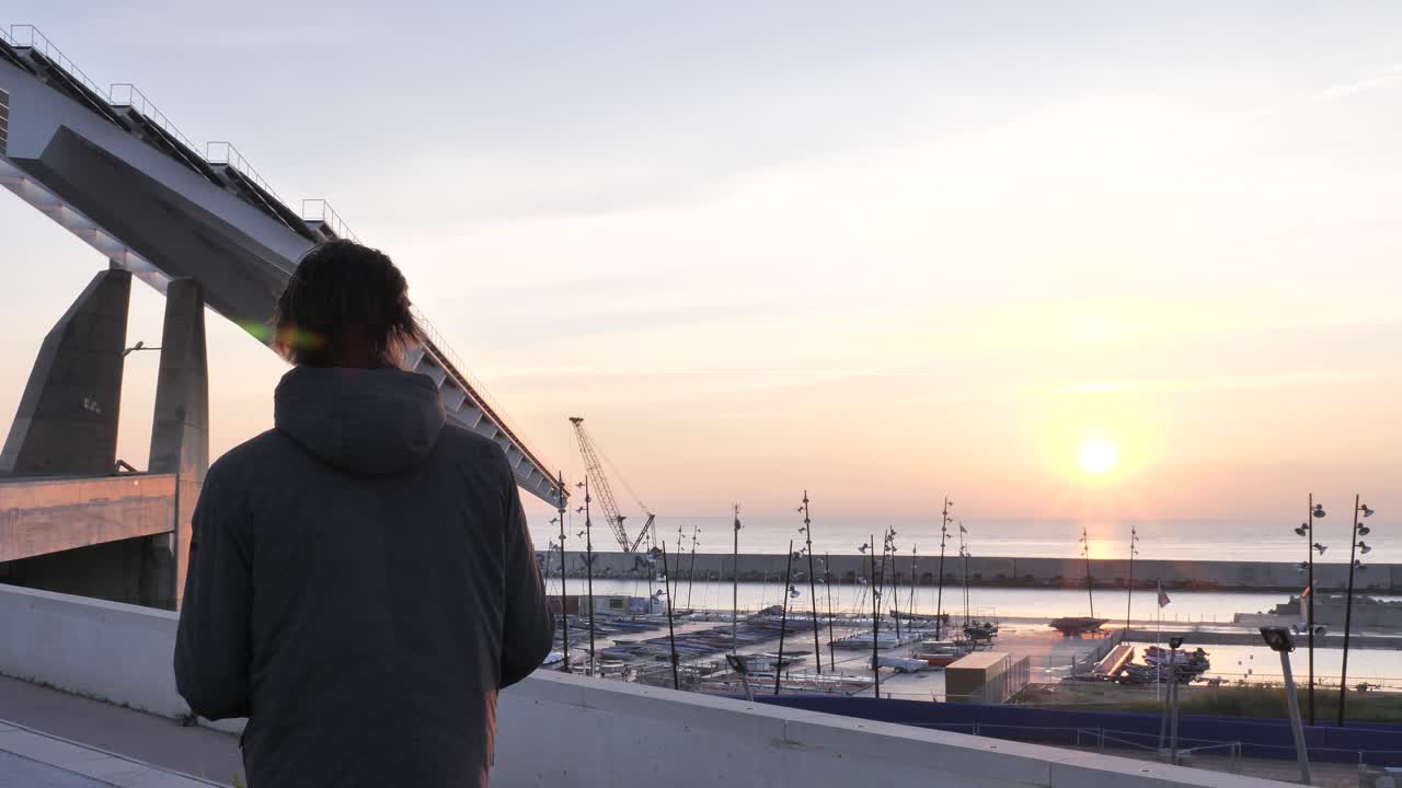 마스크를 쓴 청년은 해가 뜰 때 e스쿠터에 도착하고, 보기 위해 멈춘 다음 계속, 핸드헬드