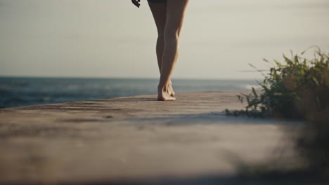 woman walking barefoot on concrete breakwater shore on bali island, dusk