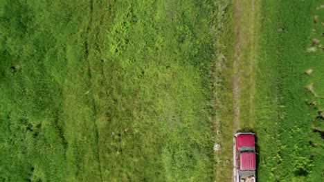 bird's eye view of a red farm truck driving on a rough road